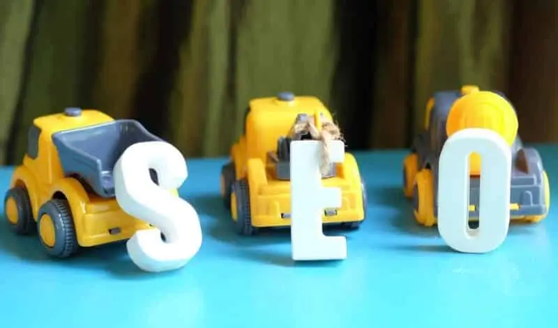 Tre camion giocattolo su una superficie blu, con le lettere S, E e O in bianco poste davanti a ciascun camion. Il primo camion ha una S davanti, il camion centrale ha una E e il terzo camion ha una O. Tende e luce della finestra sullo sfondo.